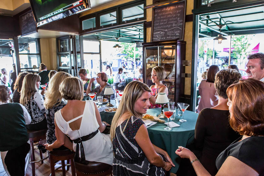 Groups of adults sitting around a bar in an open air restaurant