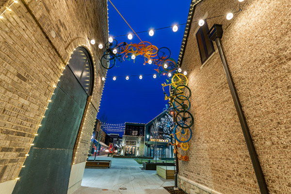 Metal sculpture of bikes in a row climbing up outdoor brick wall to connect with adjacent building.