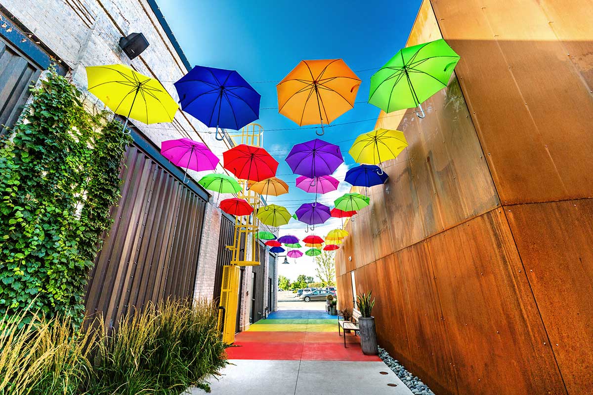 Art installation of rainbow-colored balloons over a walkway through an alley
